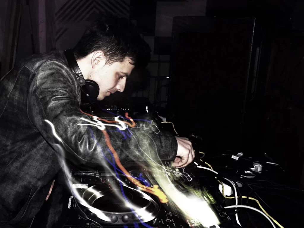 DYL working at turntables and a mixer beneath purple light trails.
