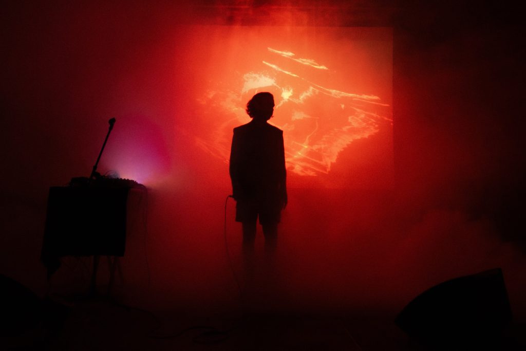 OTTOMAN GRÜW silhouetted against red and orange projections on stage.