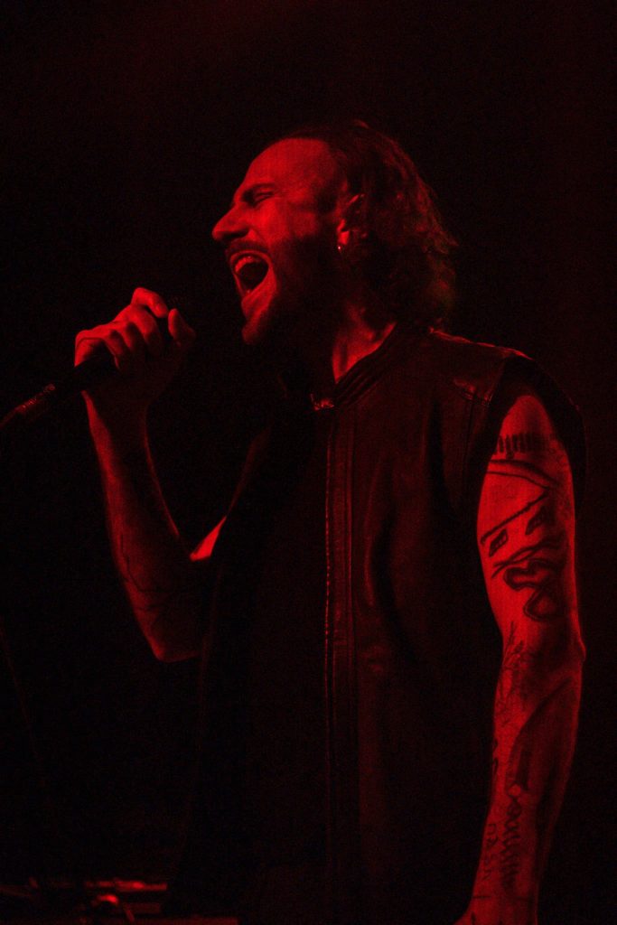 OTTOMAN GRÜW singing into a handheld microphone under red stage light.