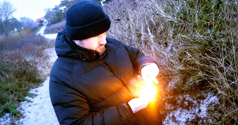 Chris Douglas outdoors in a dark winter jacket and beanie, holding a bright light