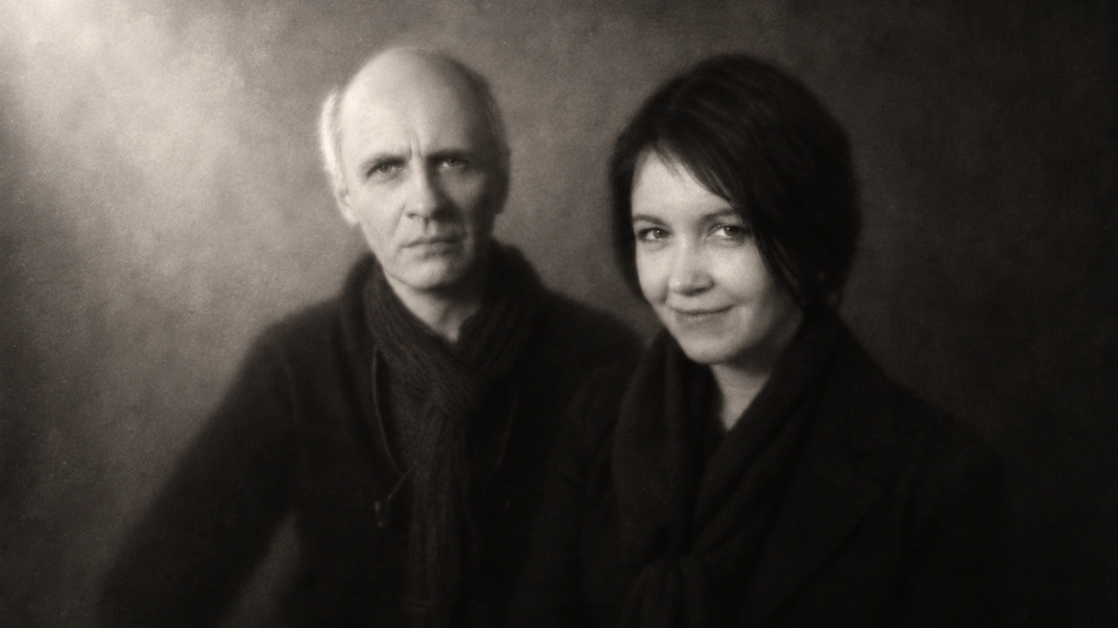 Šarūnas Nakas and Alla Zagaykevych in a softly focused monochrome portrait, wearing black scarves against a shaded wall.