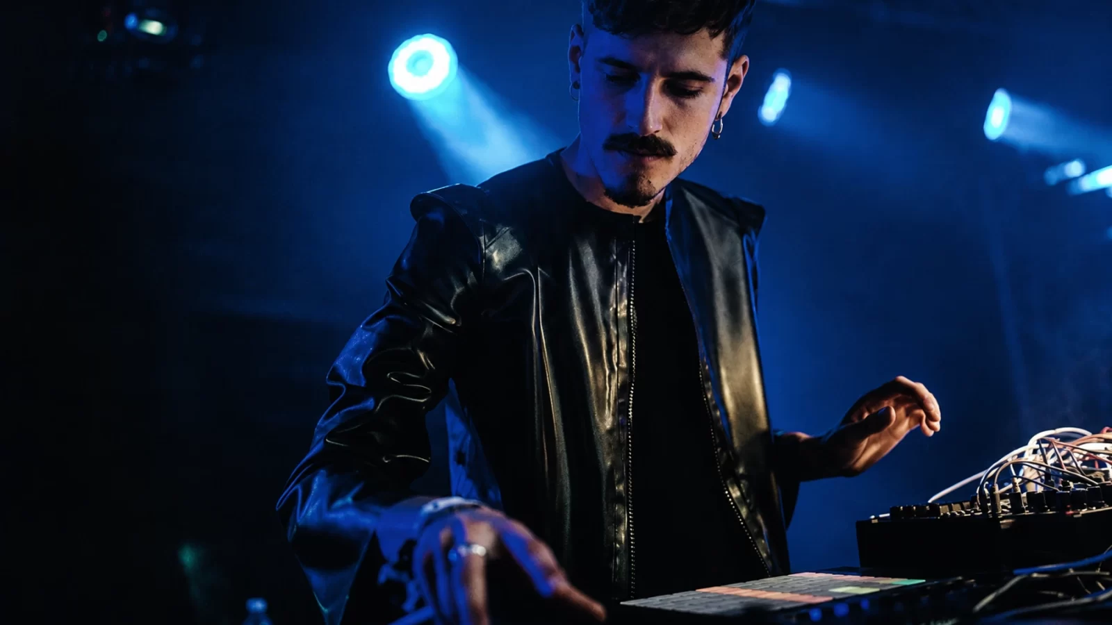 Jaroška performing with electronic equipment under cold stage light.