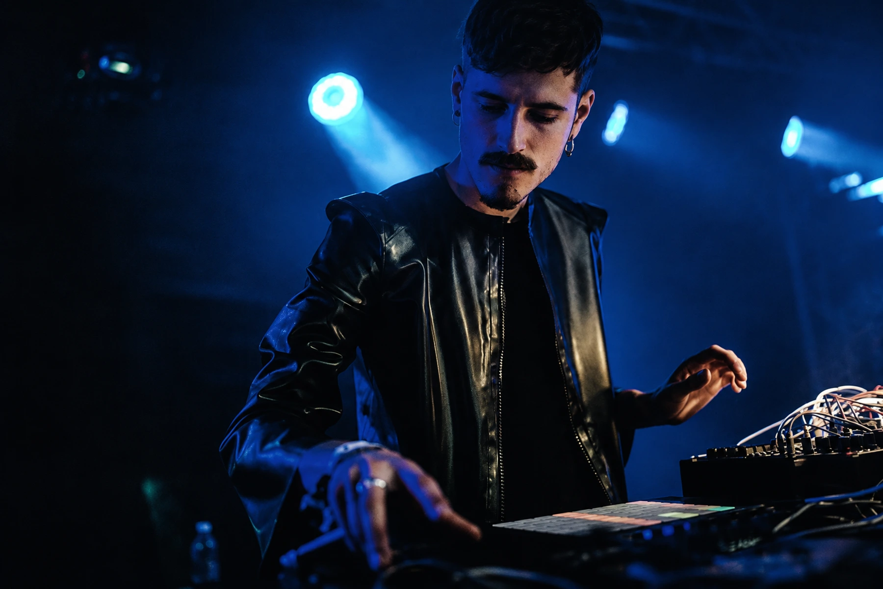 Jaroška performing with electronic equipment under cold stage light.