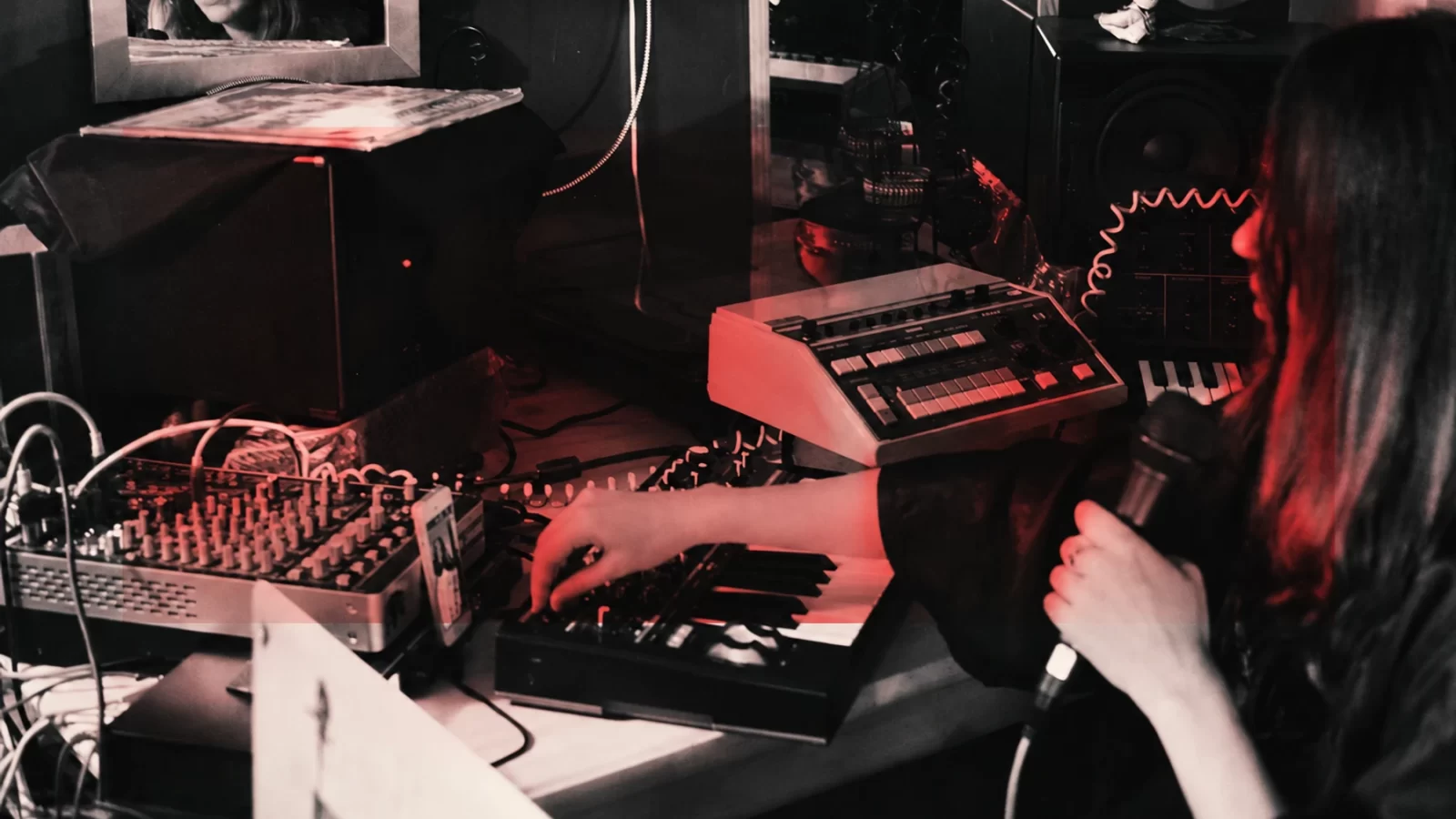 Chikiss at keyboards and a microphone in her studio, with restrained red tones.