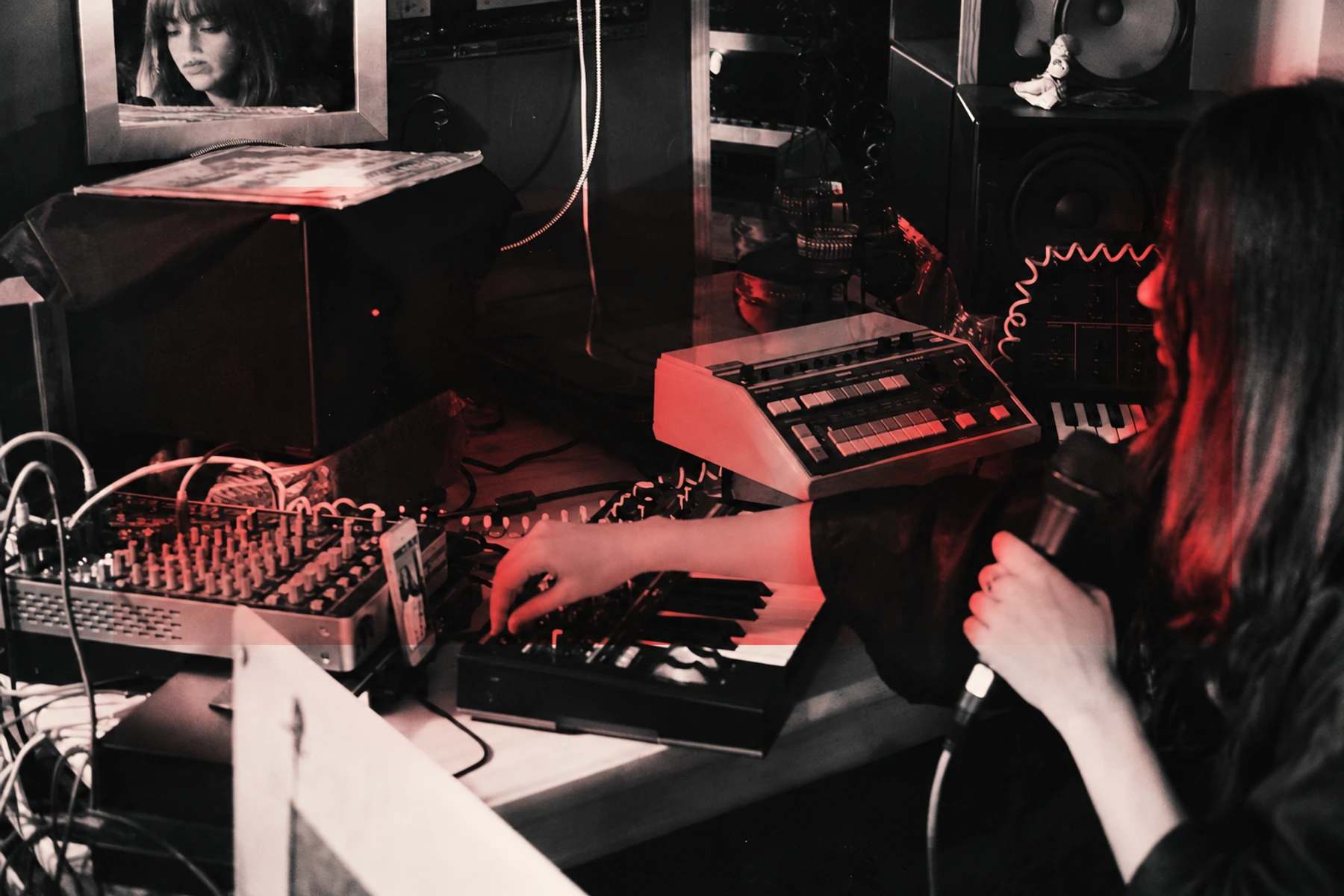 Chikiss at keyboards and a microphone in her studio, with restrained red tones.
