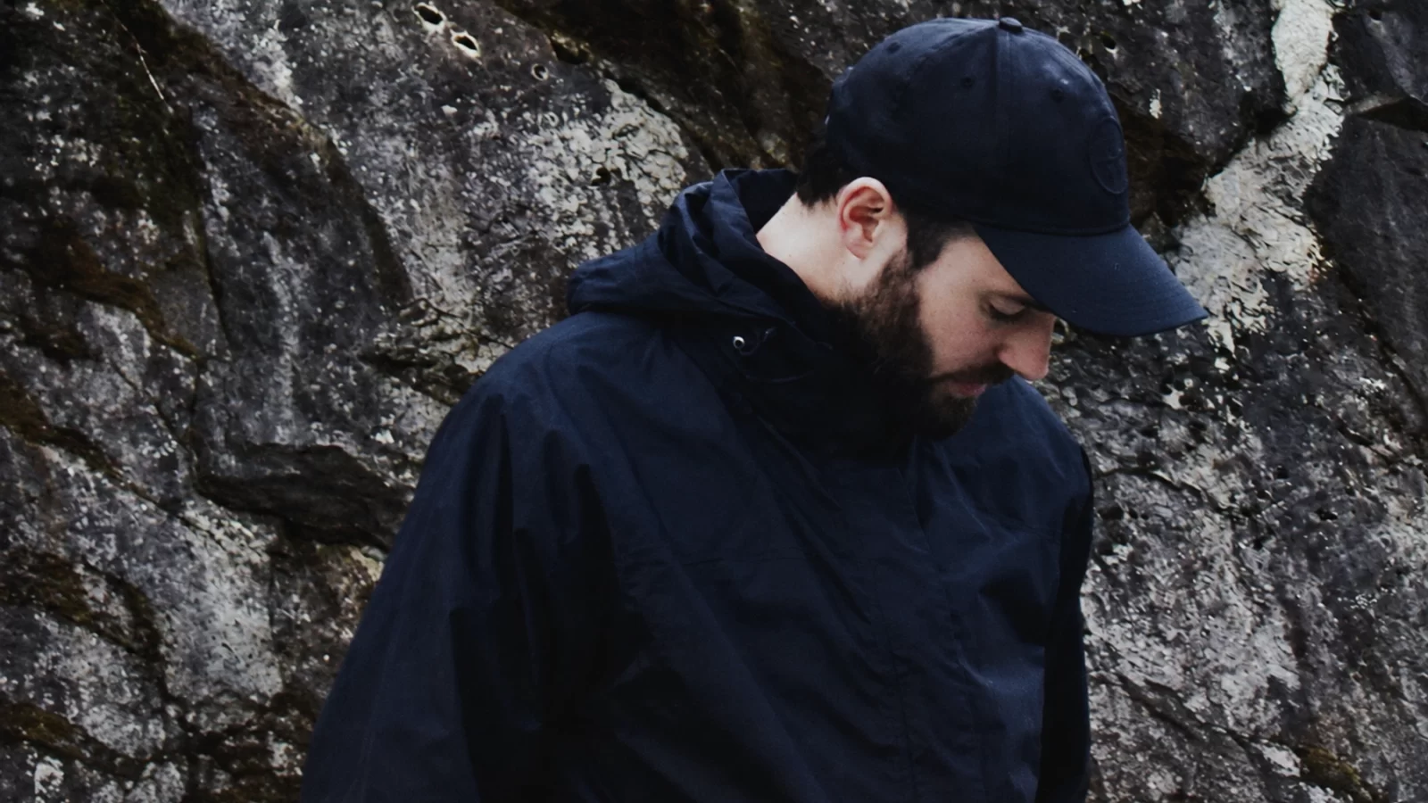 Andrea Napoli looking down beside a textured stone wall.