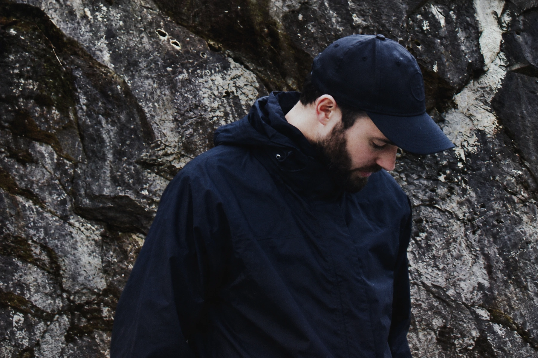 Andrea Napoli looking down beside a textured stone wall.
