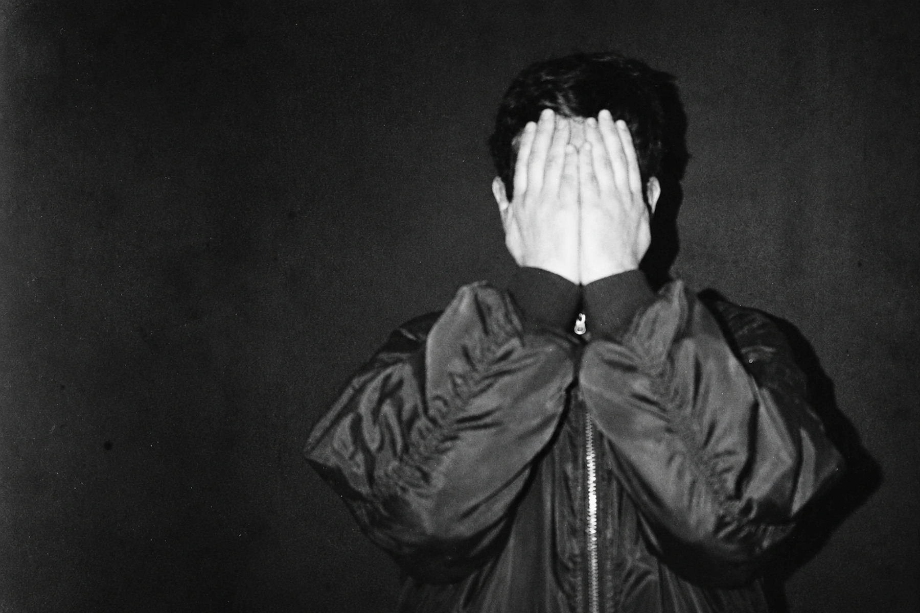 ANFS covering his face with both hands against a dark background.
