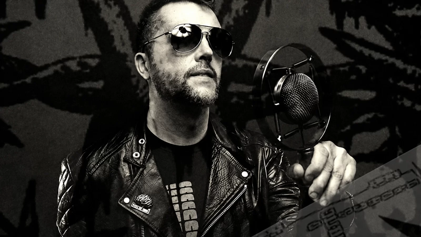 Huren in sunglasses and a leather jacket beside a microphone.