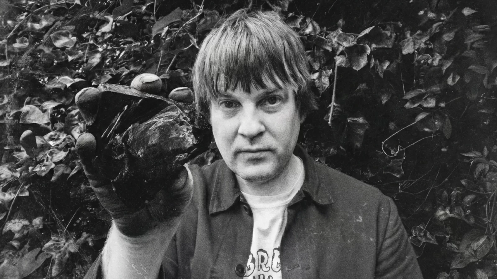 Alexander Tucker holding a dark stone beside his face, surrounded by foliage.
