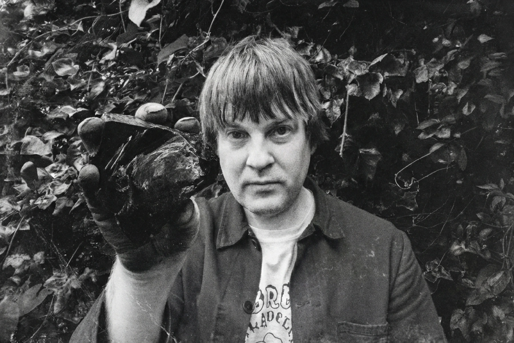 Alexander Tucker holding a dark stone beside his face, surrounded by foliage.