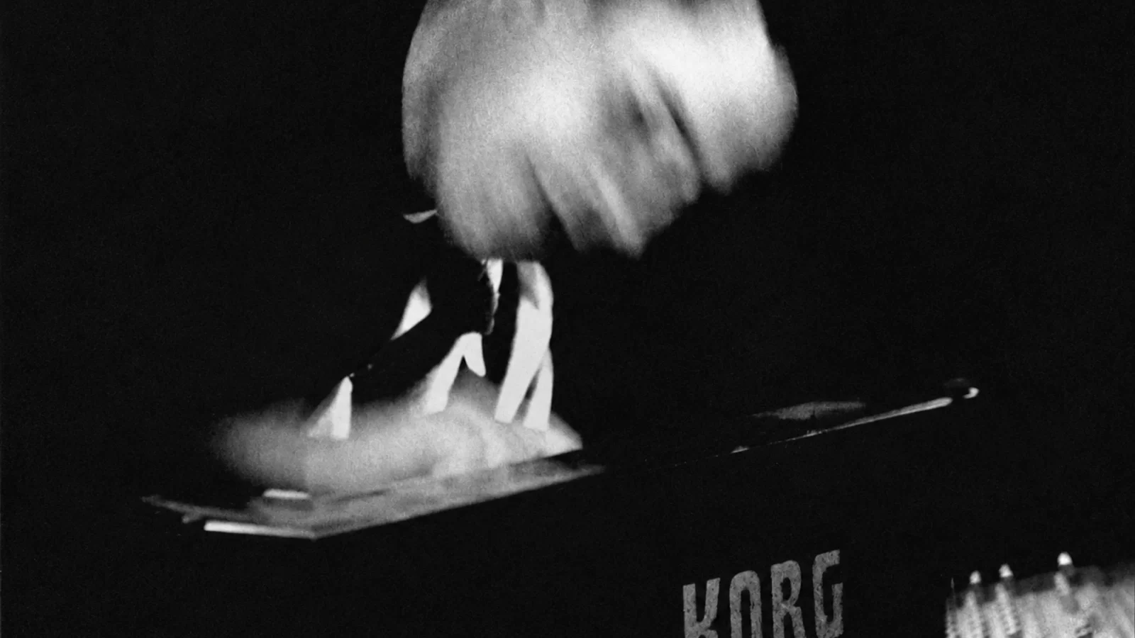 JFK performing at a Korg synthesizer, with expressive movement blur.