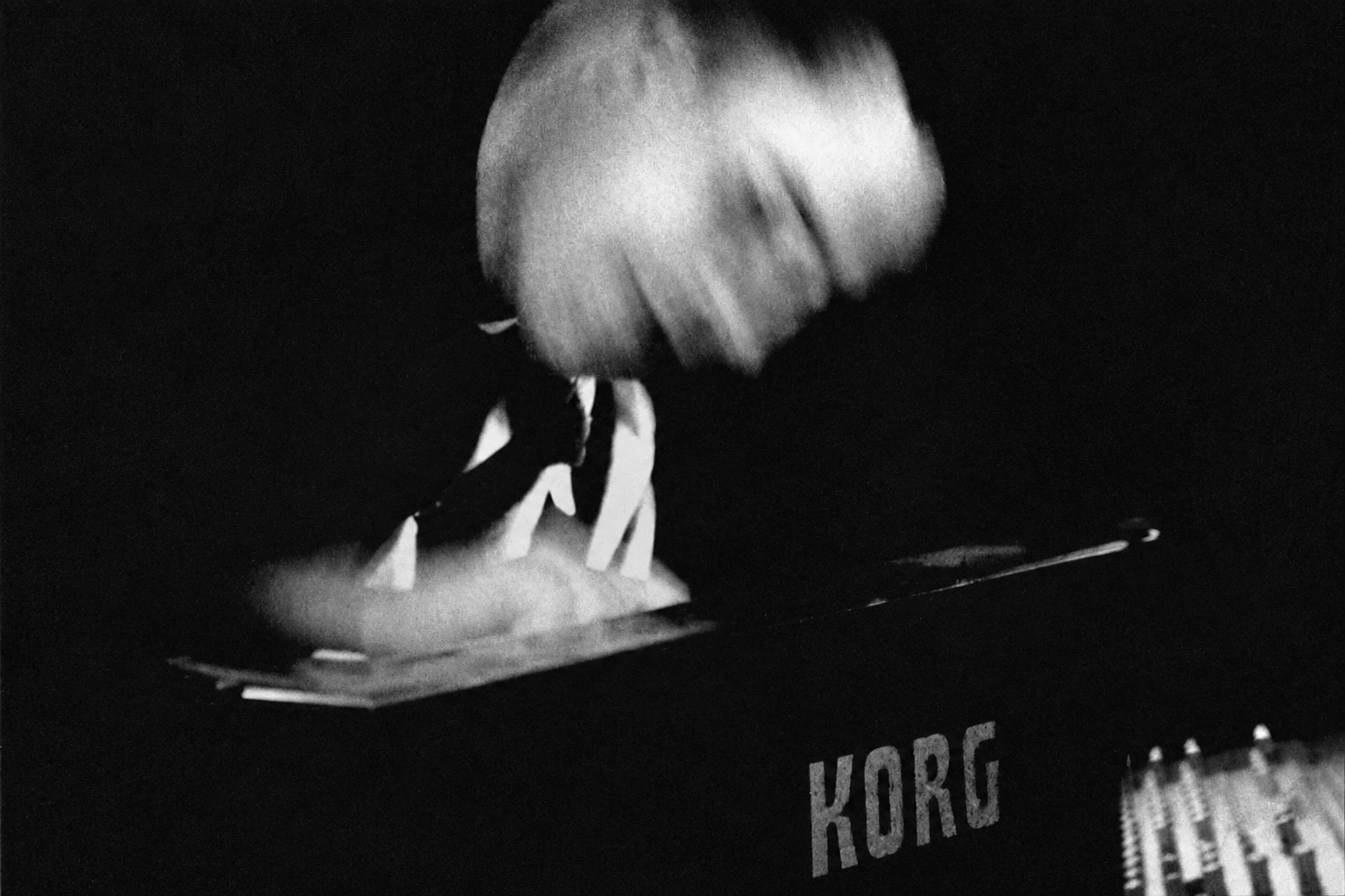 JFK performing at a Korg synthesizer, with expressive movement blur.