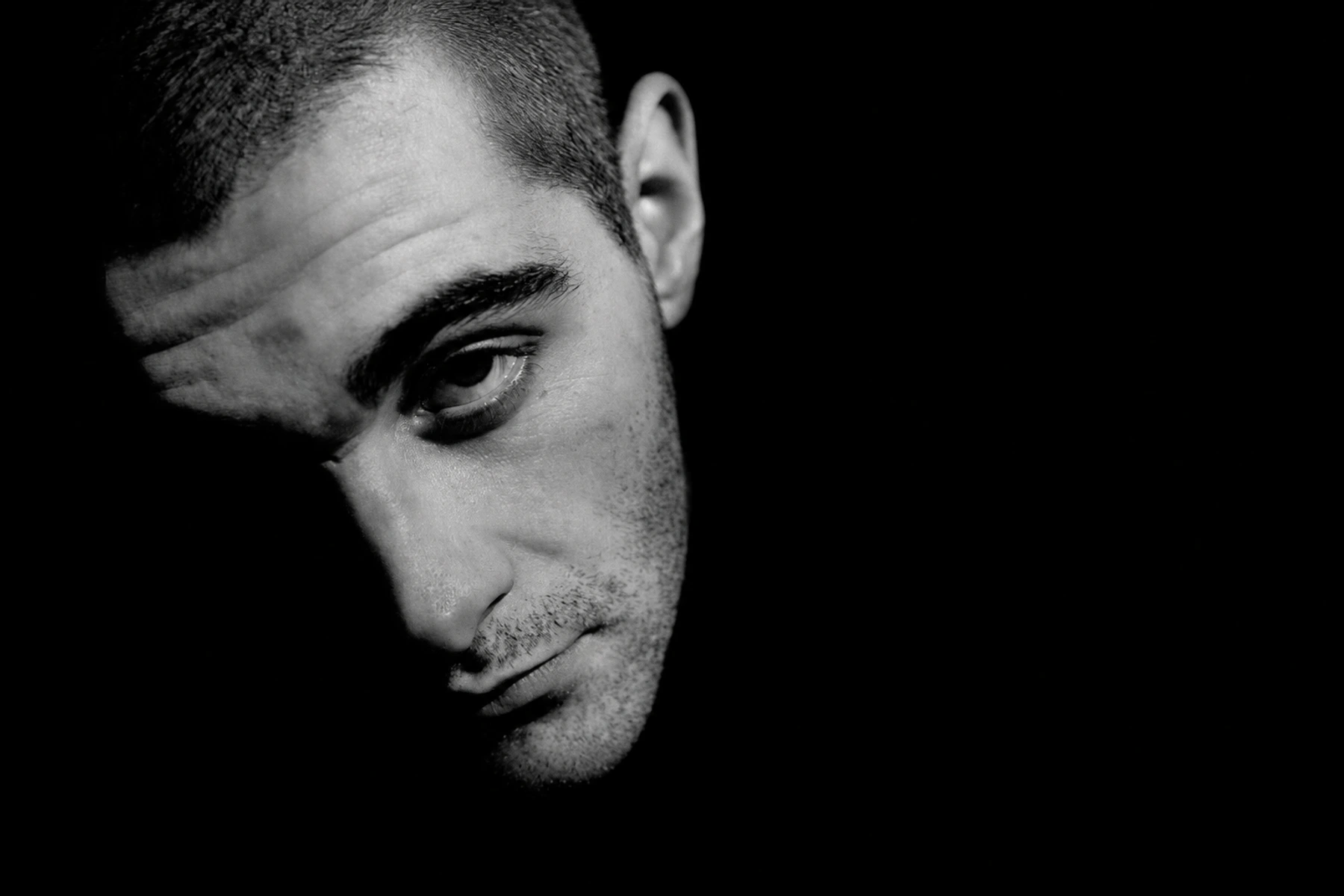 Paulie Jan’s face emerging diagonally from deep shadow in a monochrome close-up.