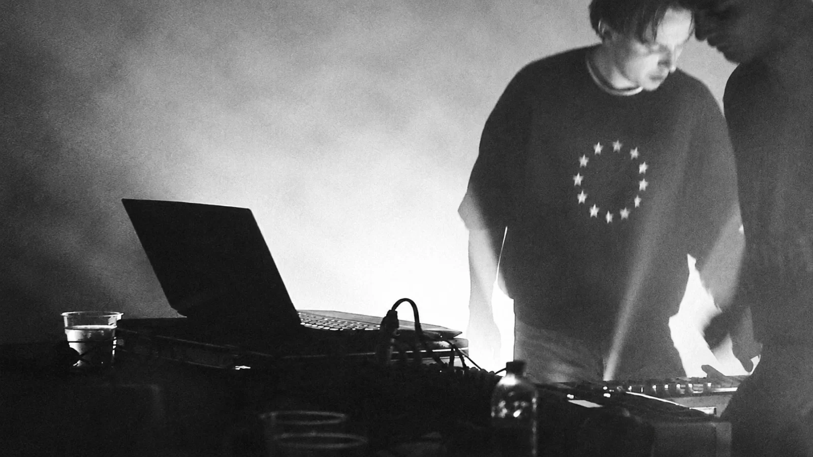 Lyra Valenza performing with a laptop and electronic instruments in a hazy room.