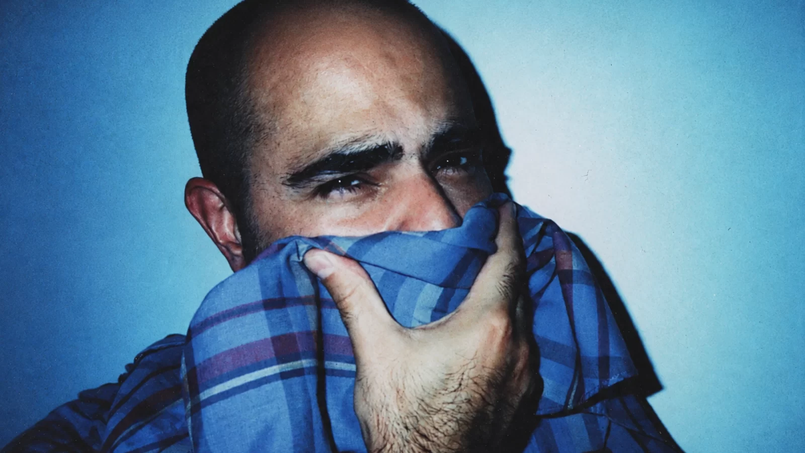 Marcos Cabral in a blue checked shirt with one hand raised to his mouth.
