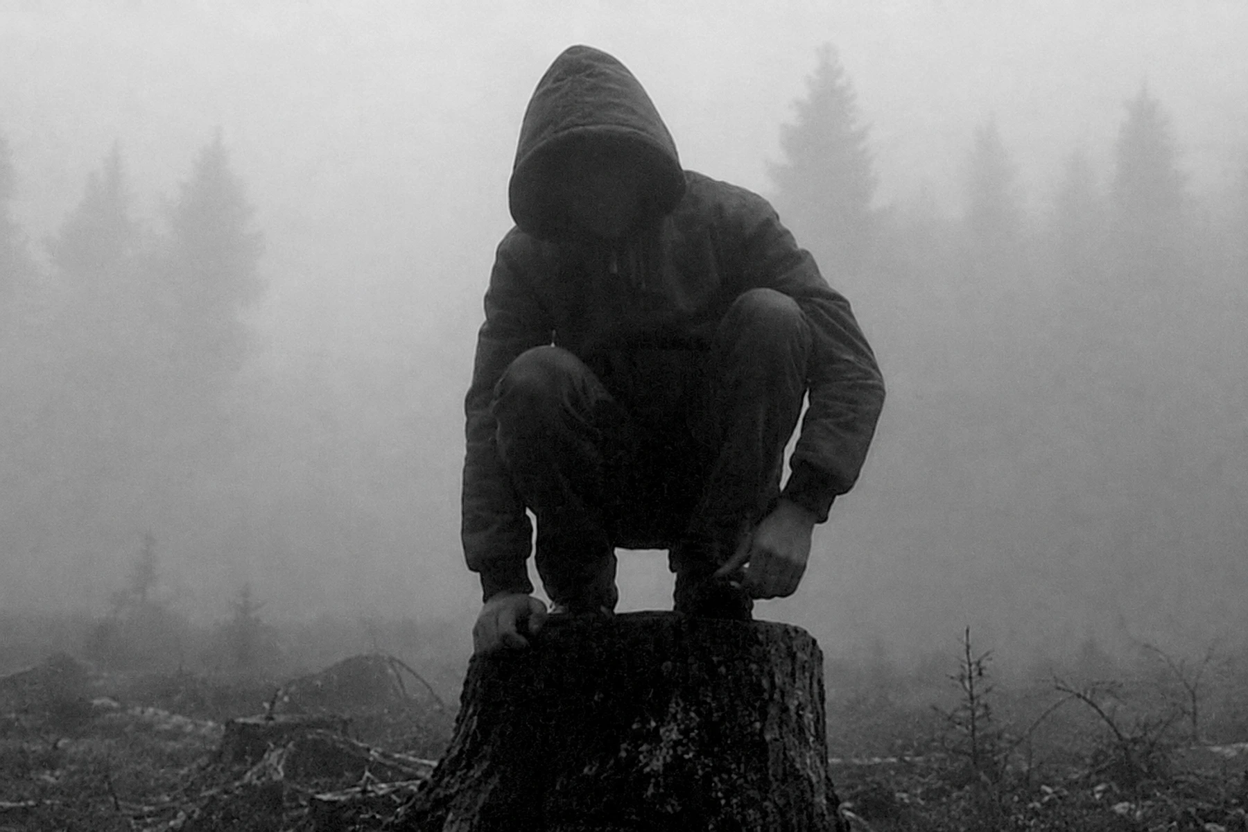 Subkutan crouching in a hooded jacket in a misty landscape.