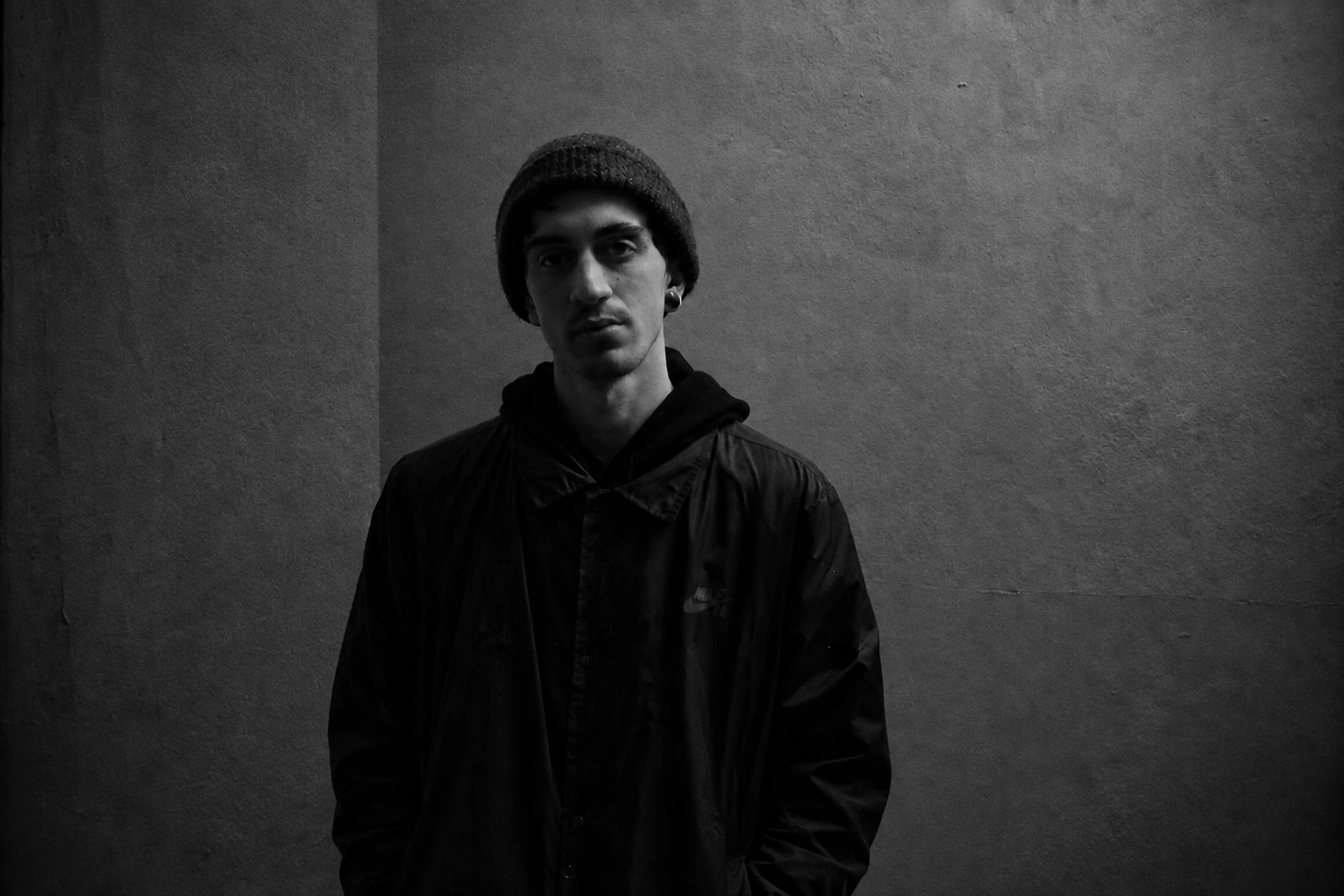 Giulio Spampinato / Coeden in a black beanie and jacket against a textured wall.