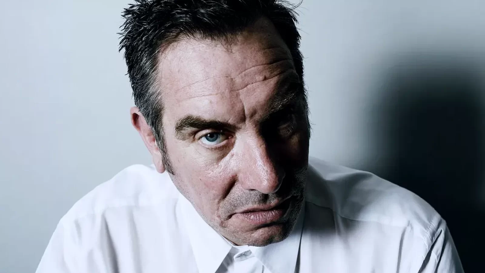 Mark Stewart wearing a white shirt, looking towards the camera.