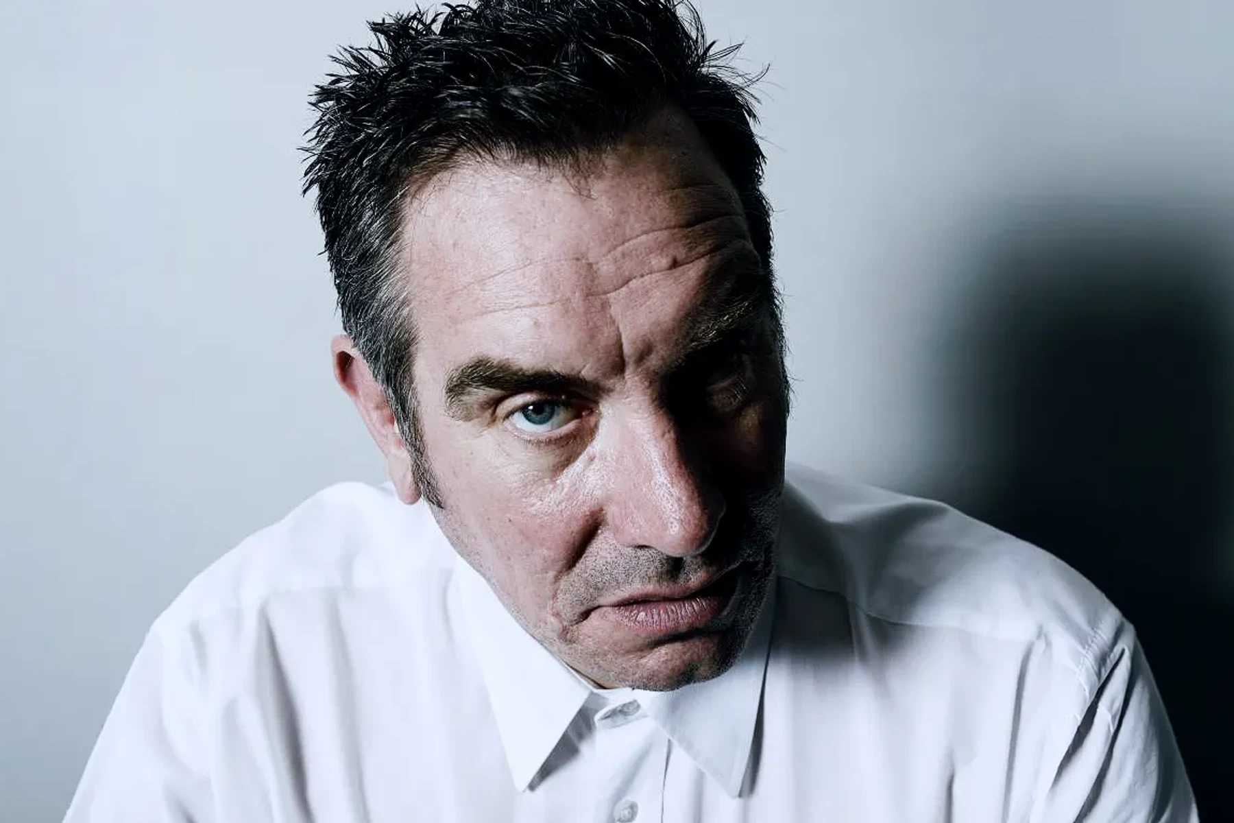 Mark Stewart wearing a white shirt, looking towards the camera.