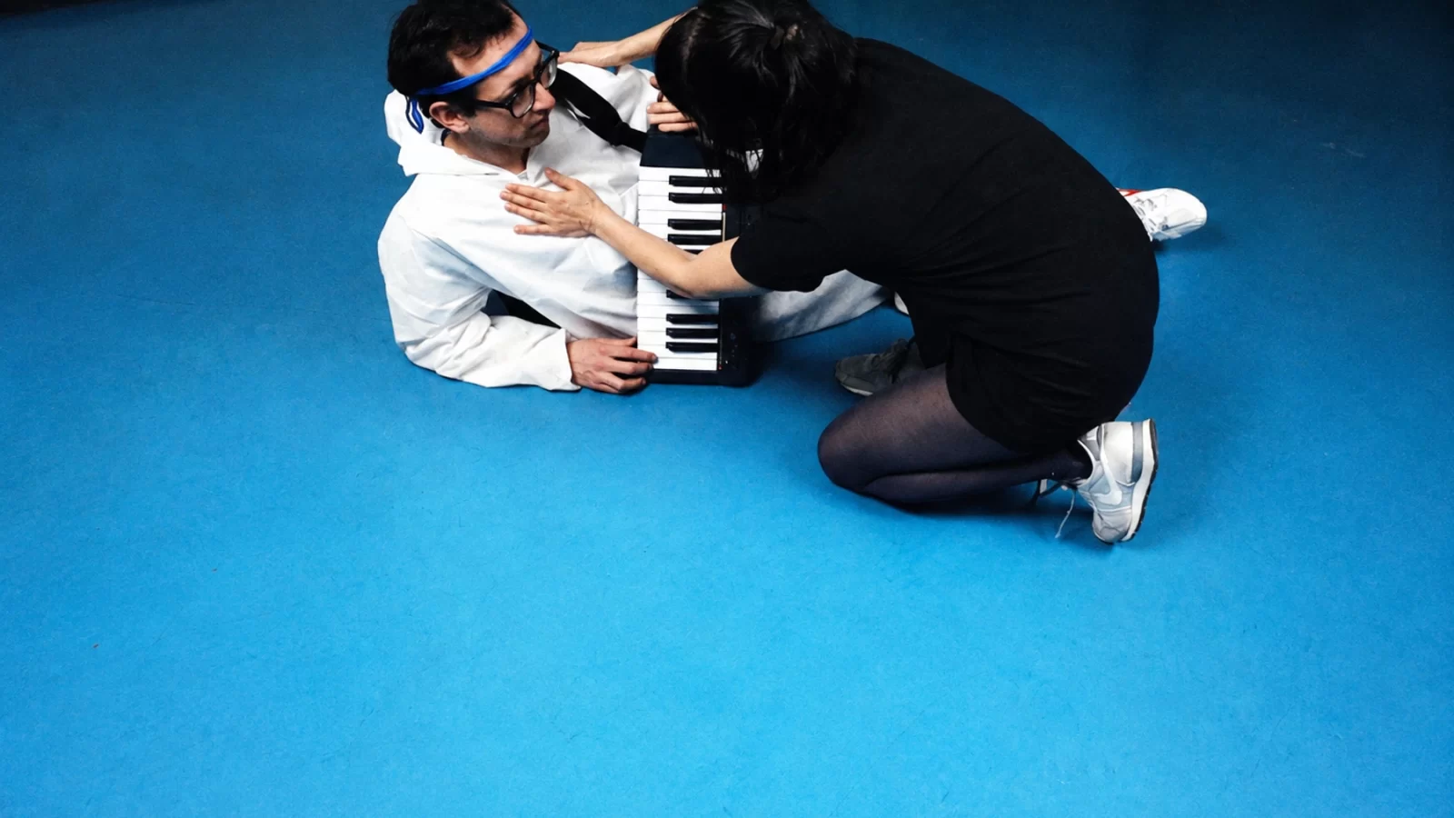 Rutger Muller / Diskette Deluxe reclining on a blue floor with a keyboard during a performance.