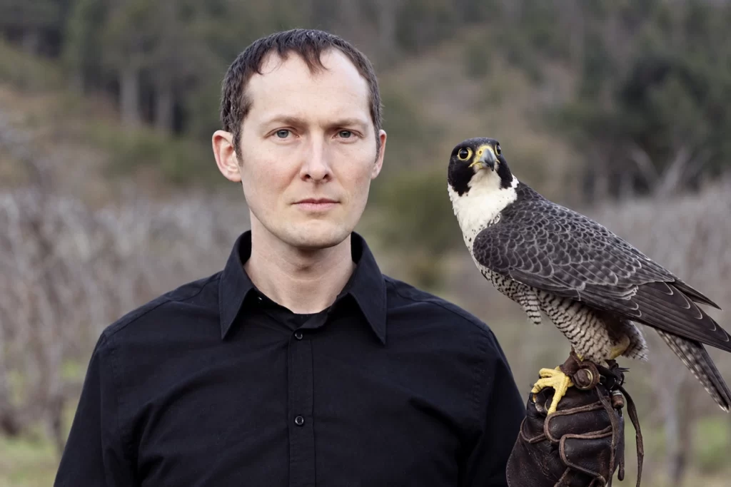 Lawrence English holding a bird of prey on a leather glove outdoors.