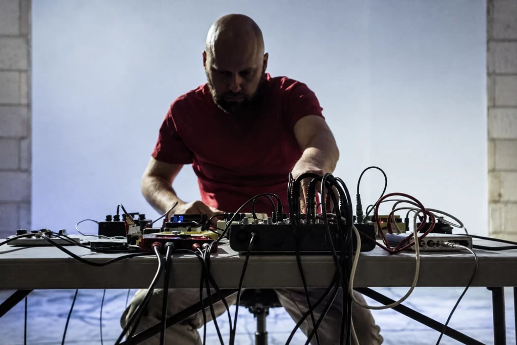 Lasse Marhaug performing over a table of electronics and cables.