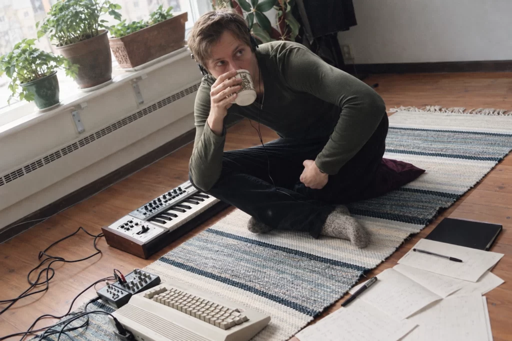 Marcus Fjellström seated with a cup beside a keyboard and plants in an archival room portrait.