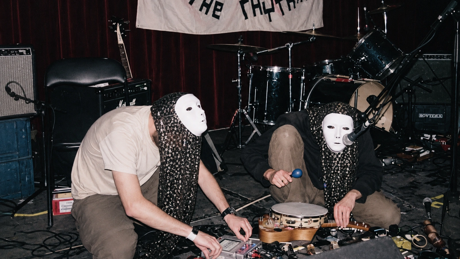 High Wolf in an archival scene with two masked figures and a patterned backdrop.