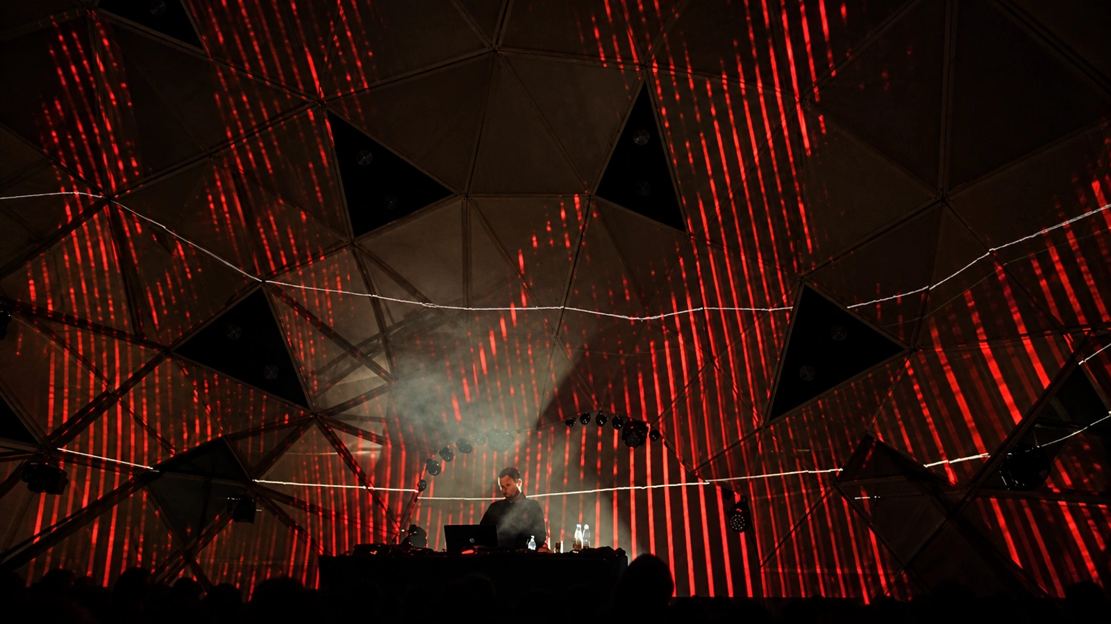 Dalglish performing beneath a geometric festival canopy filled with red striped light projections.