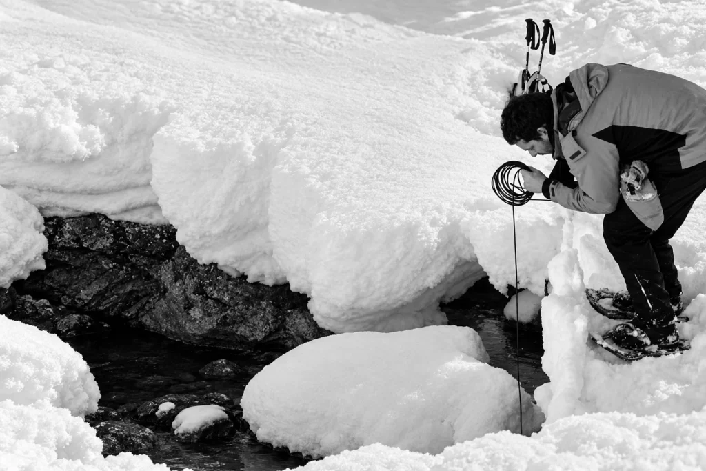 Enrico Coniglio lowering a hydrophone cable into a stream surrounded by deep snow in Cadore.