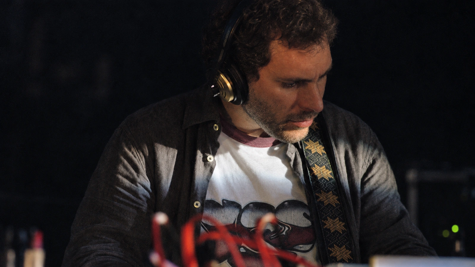 Enrico Coniglio performing with headphones, an instrument strap and red cables in the foreground.