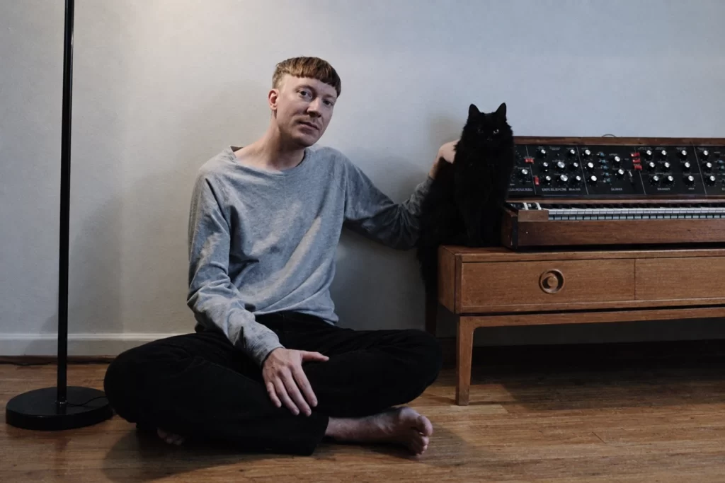 Andreas Tilliander seated beside a black cat and analog synthesizer in his studio.