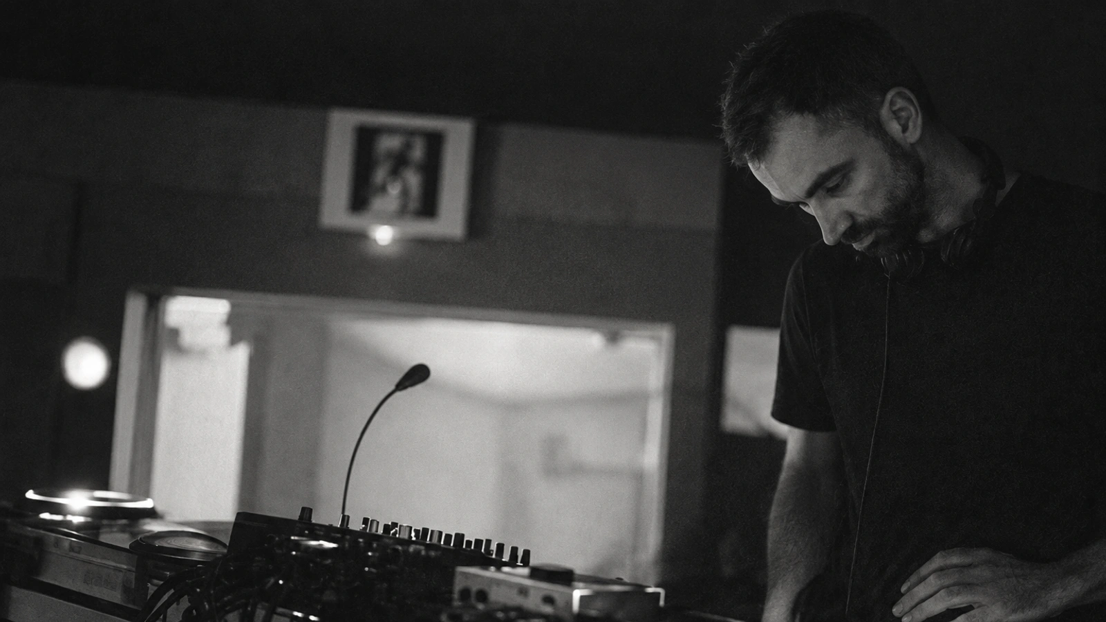 Chris Hobson of MNML SSGS looking down at turntables in a dim interior, photographed in black and white.
