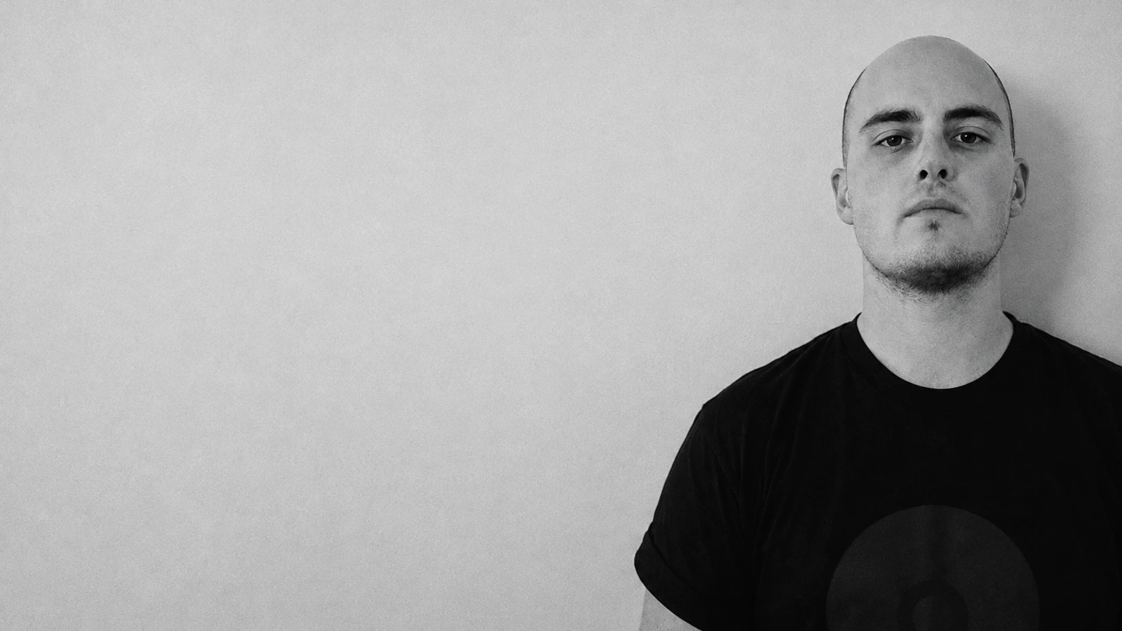 Ryan Griffin in a black shirt against a cool grey wall, in a softly lit monochrome portrait.