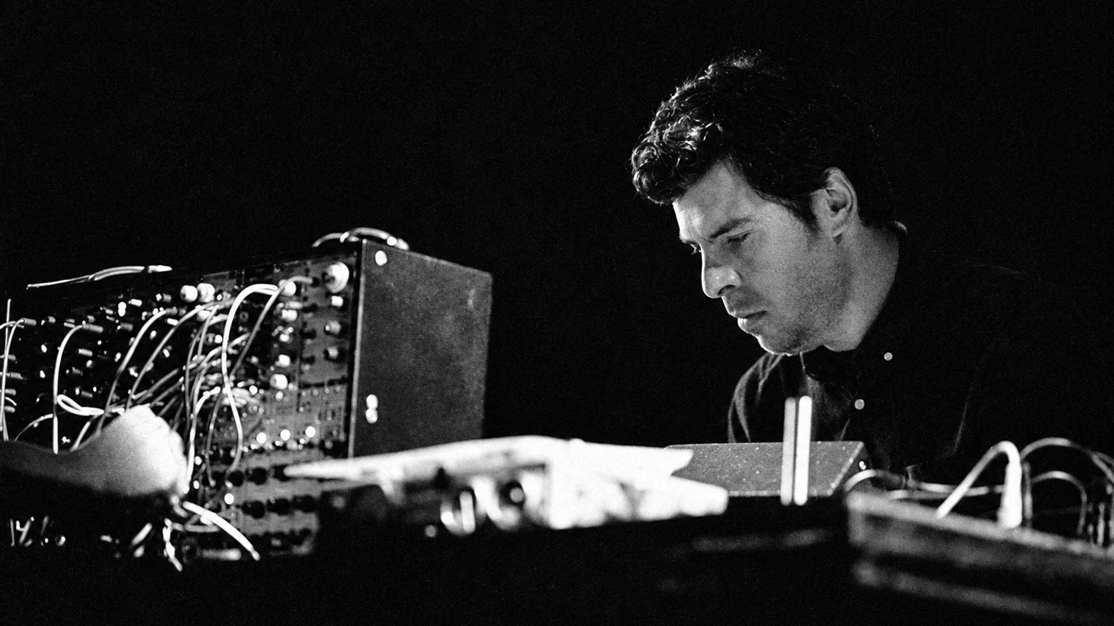 Andrew Pekler working at his synthesizer in a grainy monochrome performance photograph.
