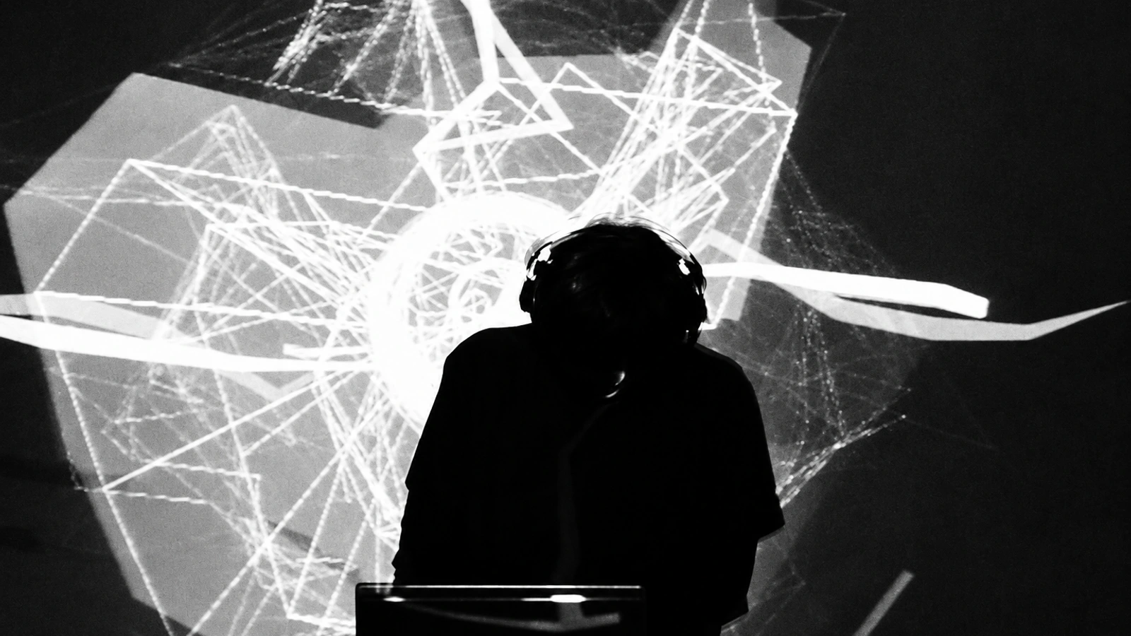 Yaporigami wearing headphones in silhouette before an angular monochrome projection.