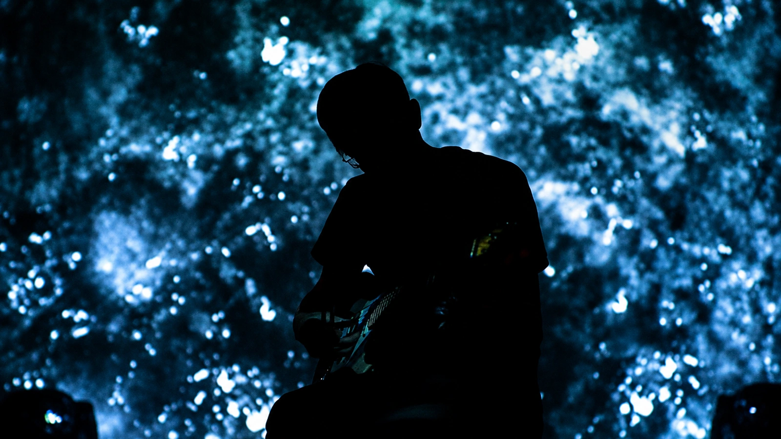 Svarte Greiner performing as a dark silhouette against a textured blue and cyan projection.