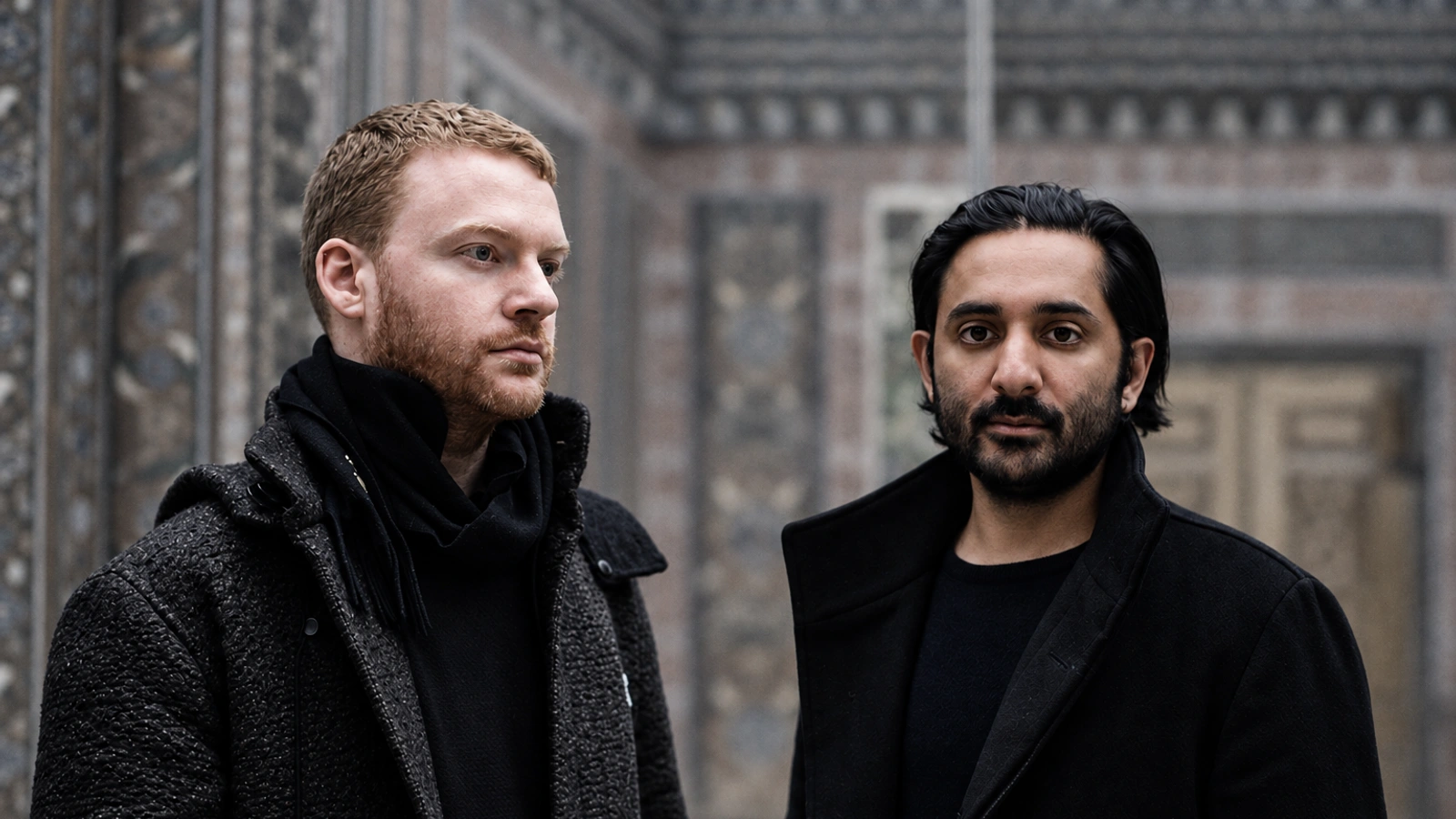James Ginzburg and Paul Purgas of Emptyset in dark coats against a muted industrial brick and steel backdrop.