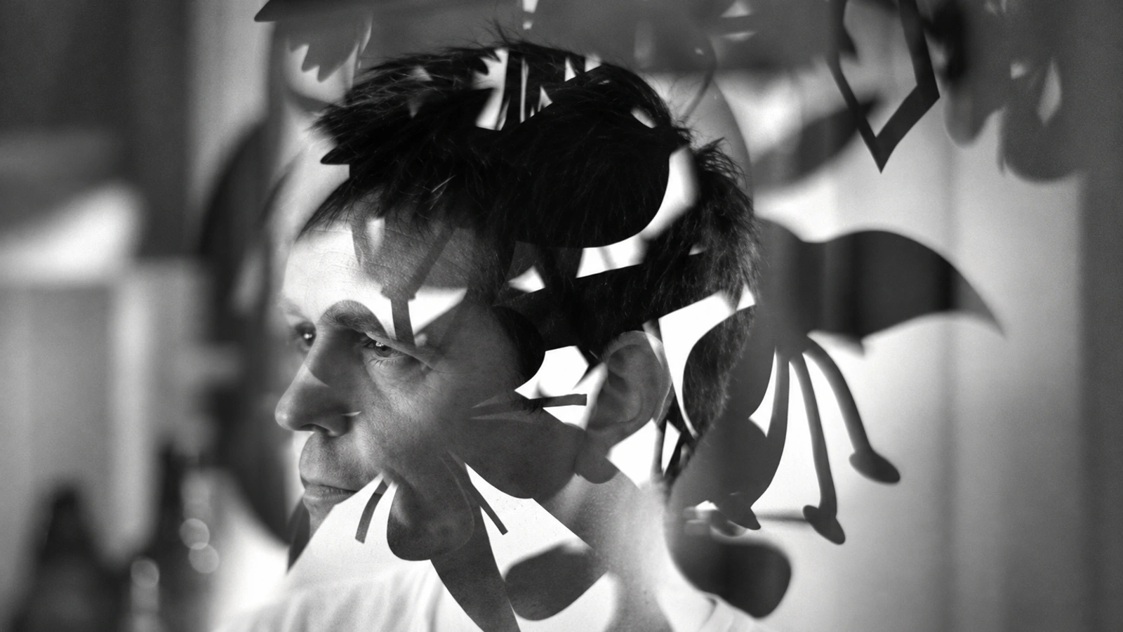Simon Scott in profile behind overlapping abstract shapes, in a monochrome photograph.