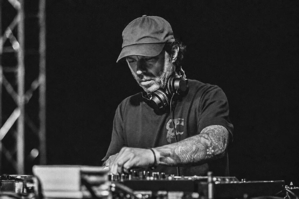 Presha performing with headphones around his neck, hands on the decks, in a grainy monochrome photograph.