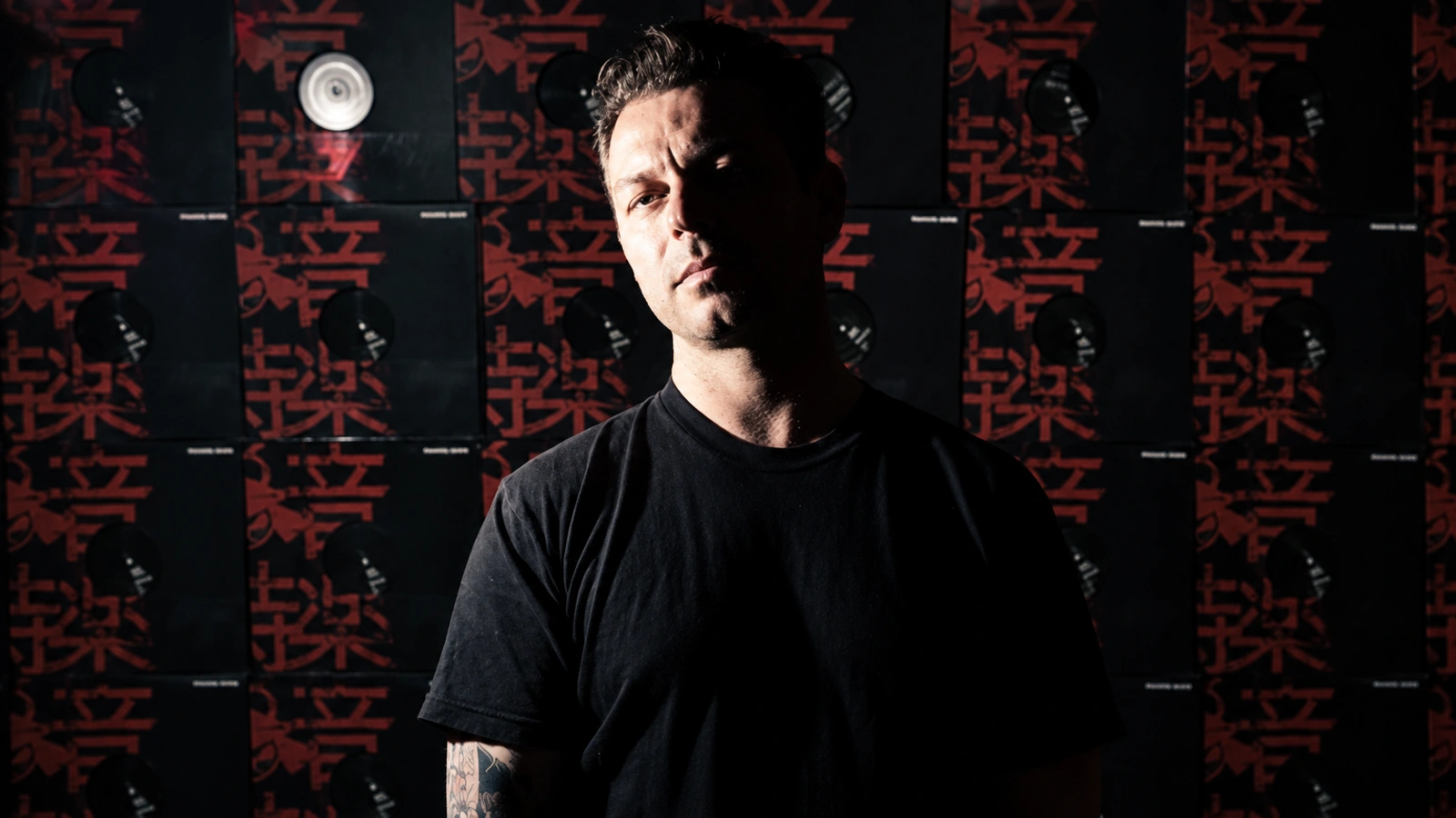 Presha in a dark portrait against a wall of red and black record sleeves.