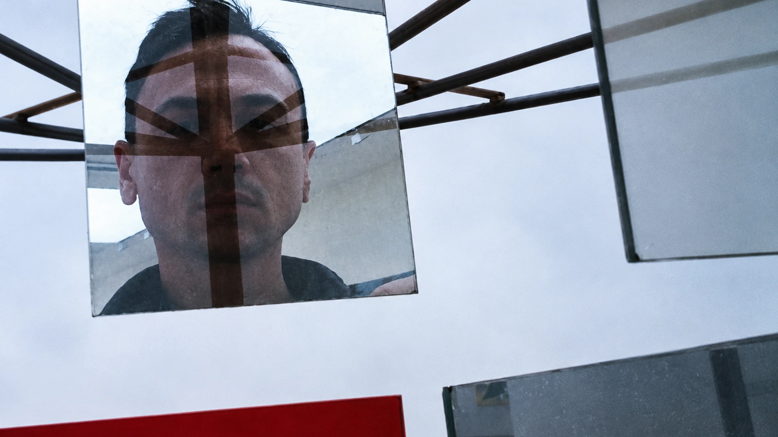 Gintas K reflected behind geometric glass panels and dark horizontal bars.