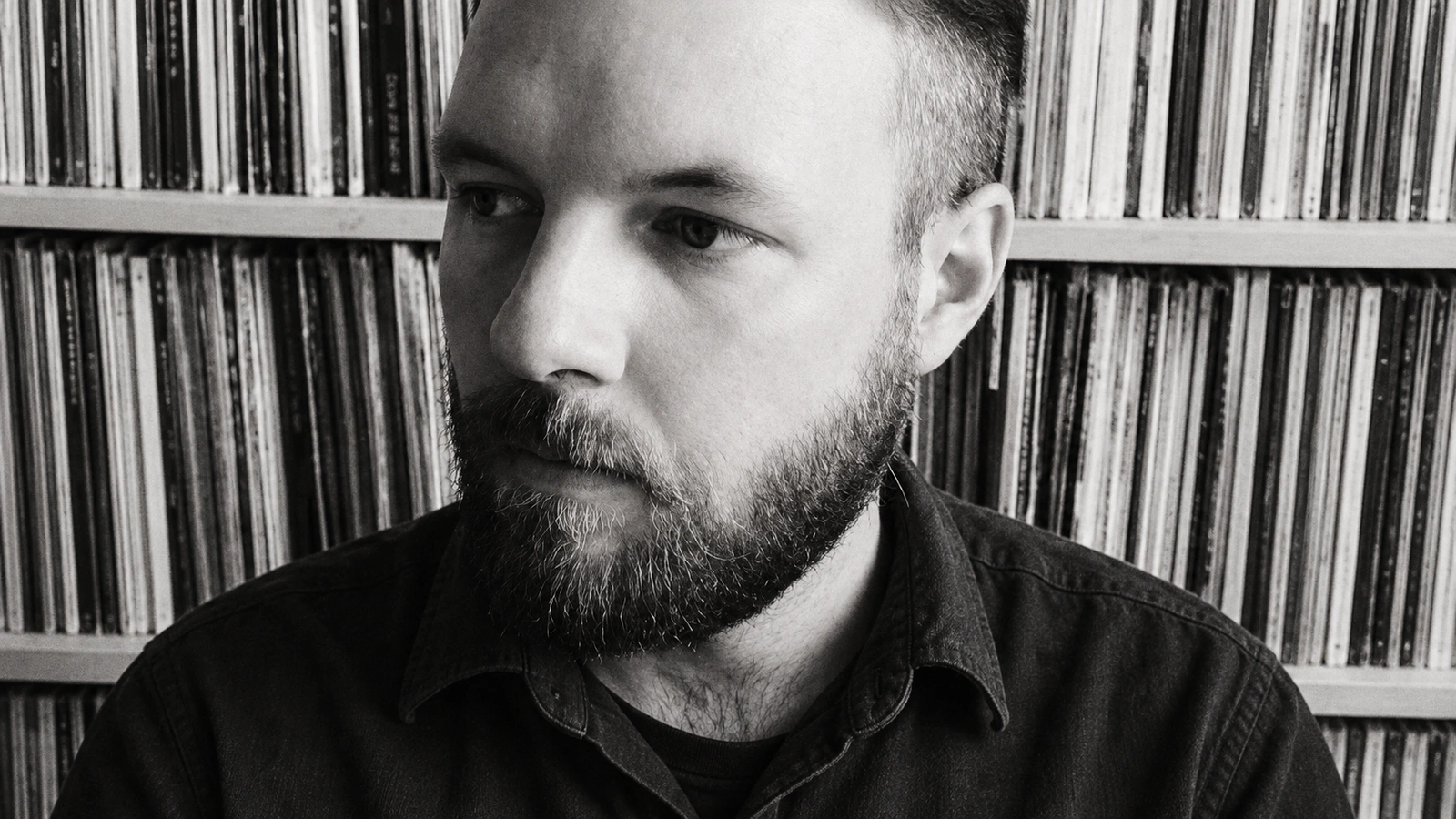 Koen Holtkamp in a monochrome portrait against shelves of records, wearing a plain dark shirt.