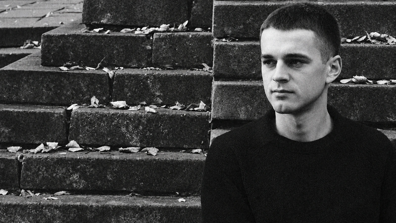 Aerobica sitting beside stone steps in a grainy monochrome portrait.