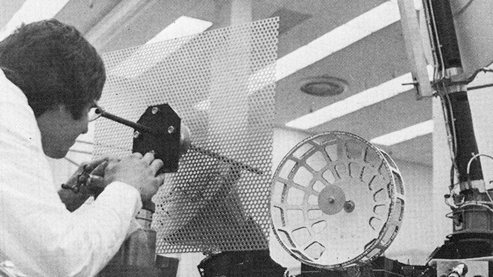 Jan Jelinek looking through a film apparatus beside a large reel, in a monochrome halftone scan.