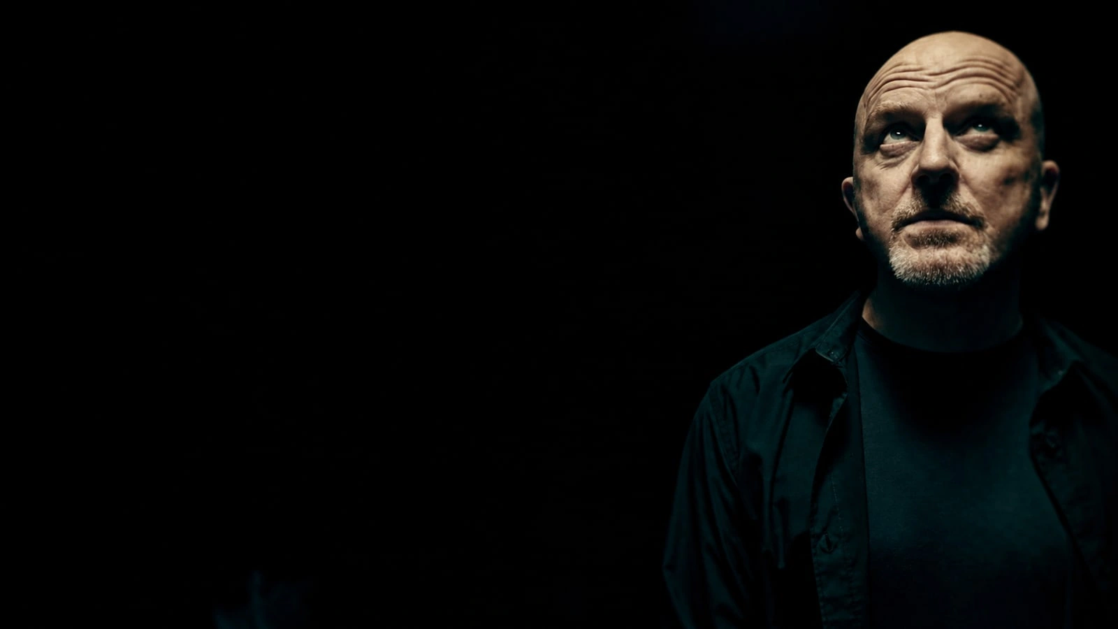 Lustmord in a dark portrait, his face lit against a black background.