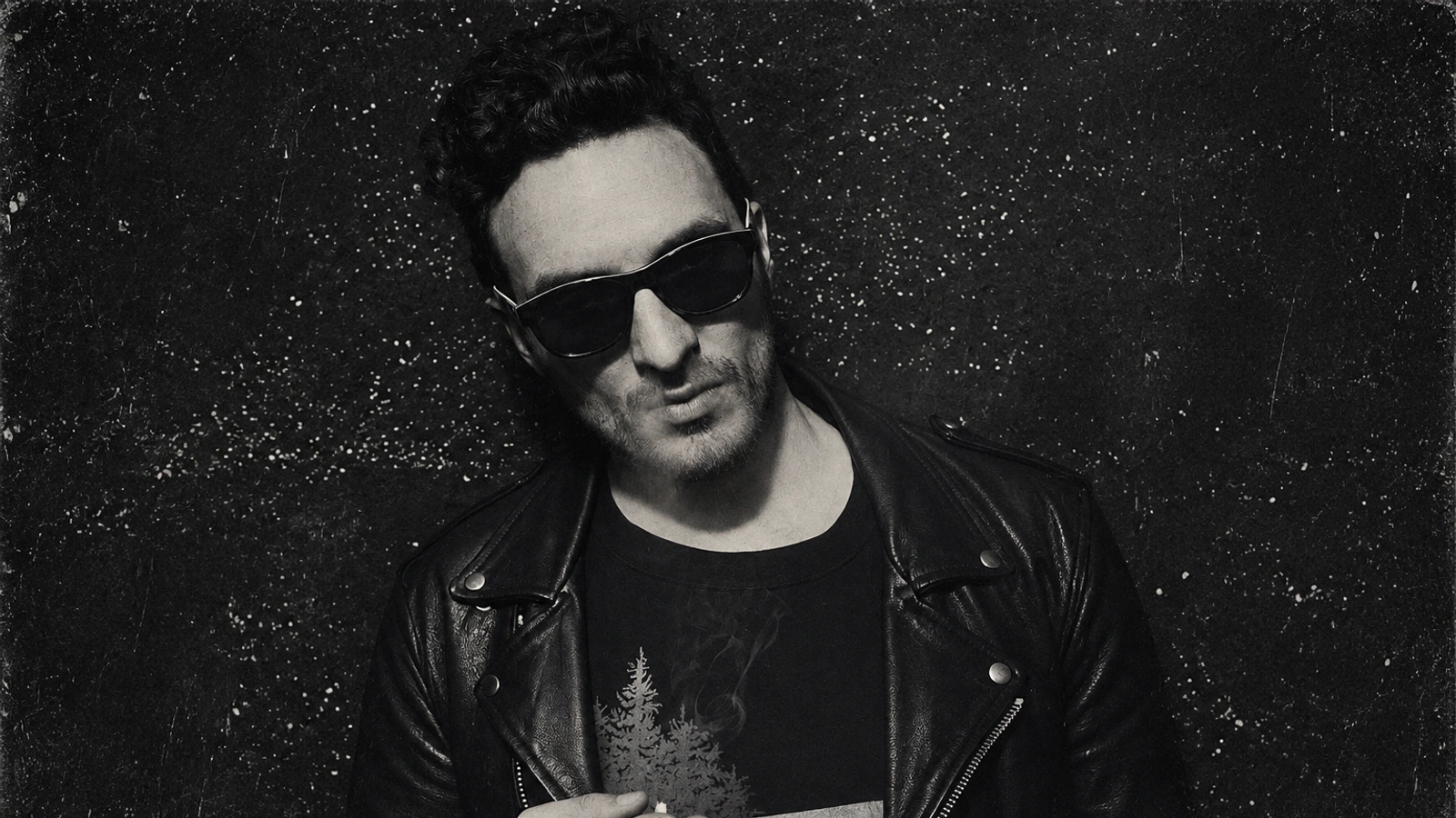Ernestas Sadau in sunglasses and a leather jacket against a textured dark wall.