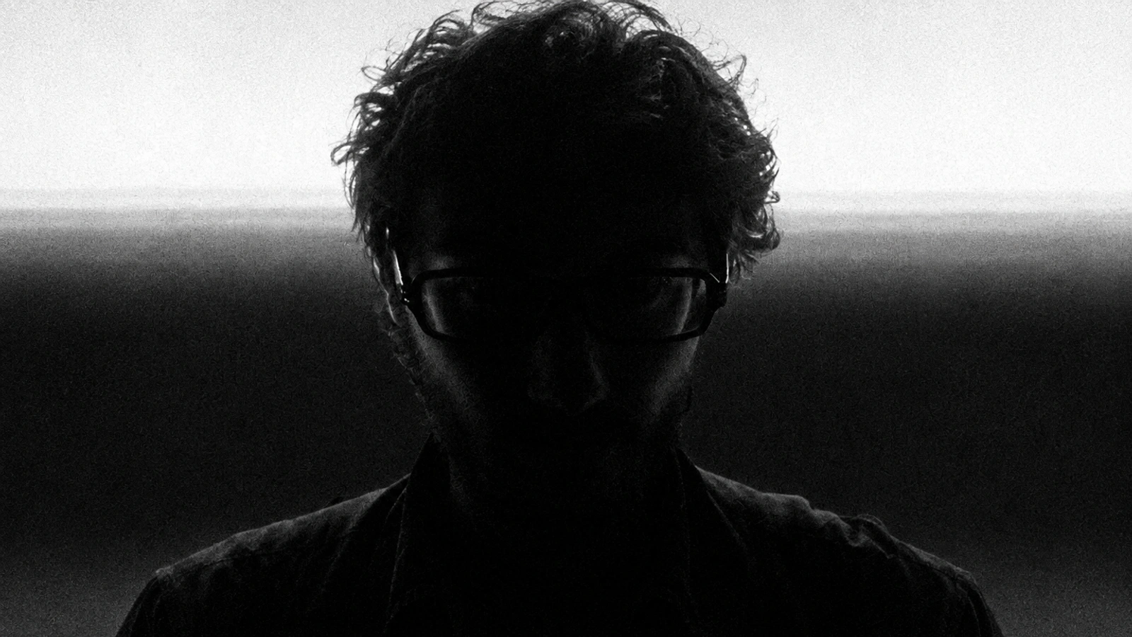 Mace. in deep shadow, with glasses silhouetted against a horizontal band of light.