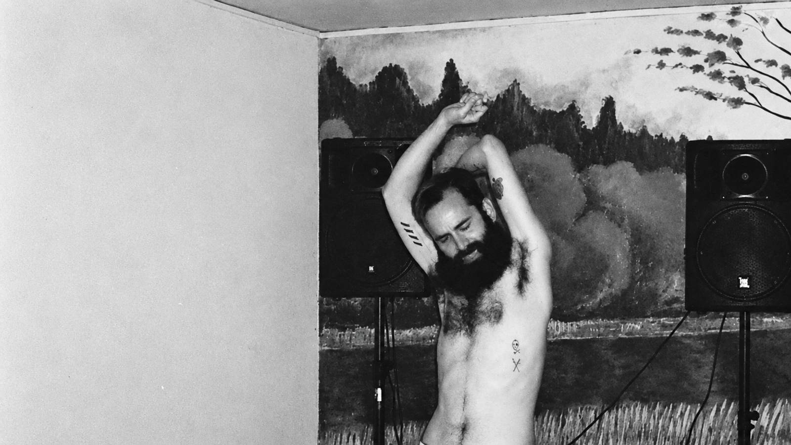 Peder Mannerfelt with raised arms between loudspeakers and a painted wall.